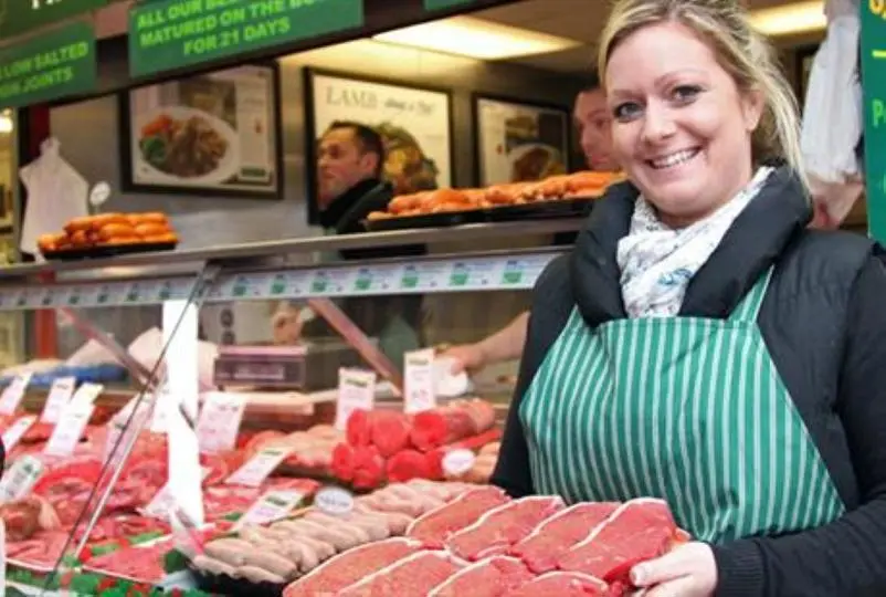 A lady stood next to the meat counter holding a tray of steaks